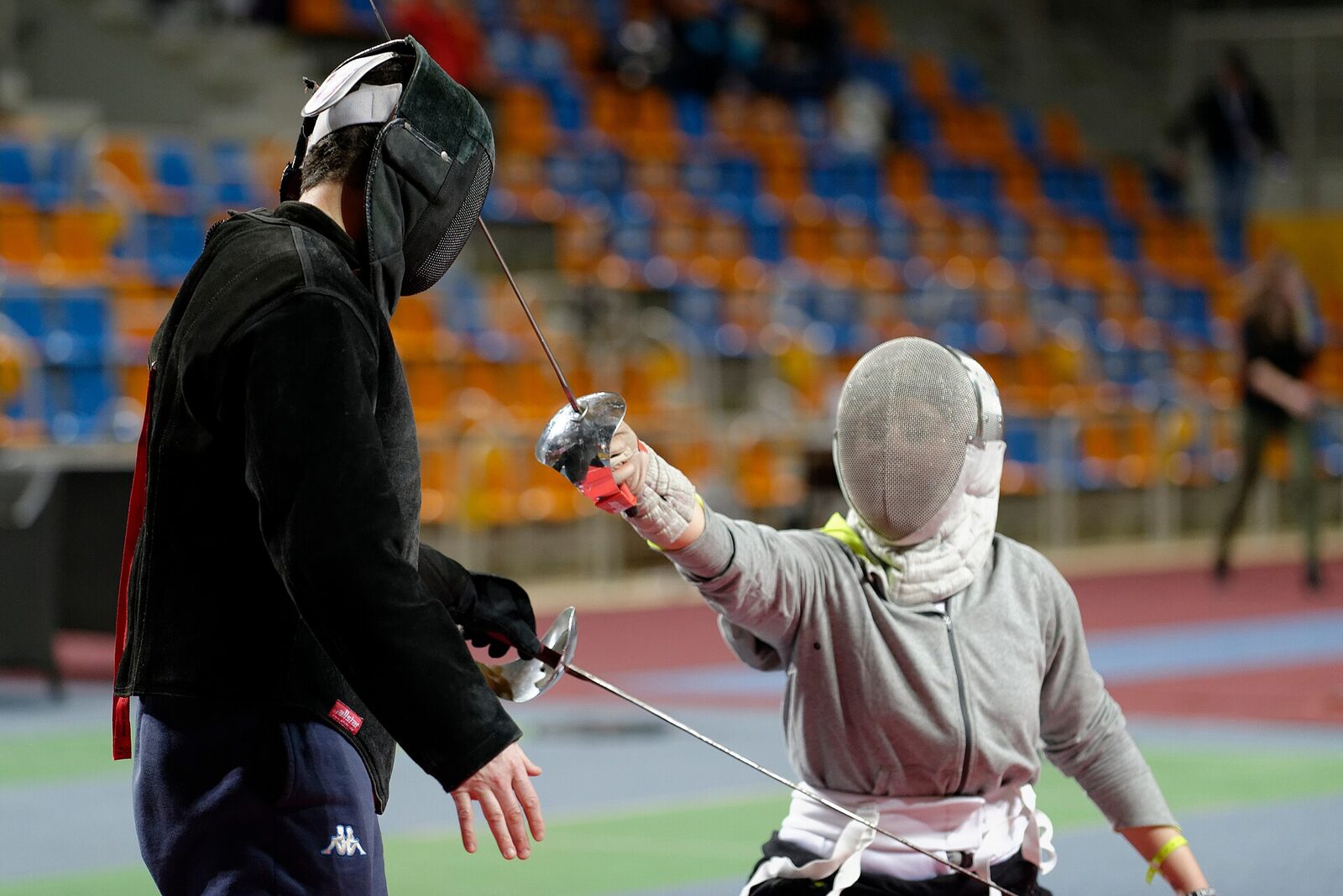 A coach in a black teaching jacket gives a fencer a one-on-one saber lesson